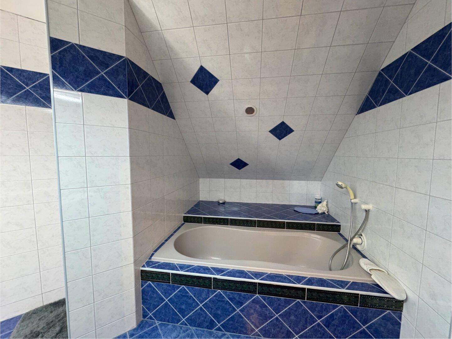 Badezimmer mit blauen und weißen Fliesen, Badewanne und Dachschräge.