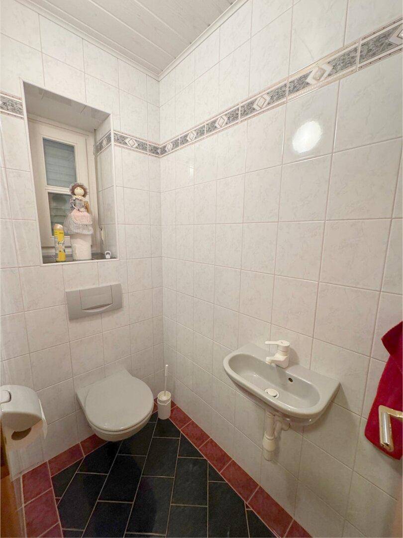 Helles Gäste-WC mit Waschbecken, Toilette und Fenster für natürliche Belüftung.