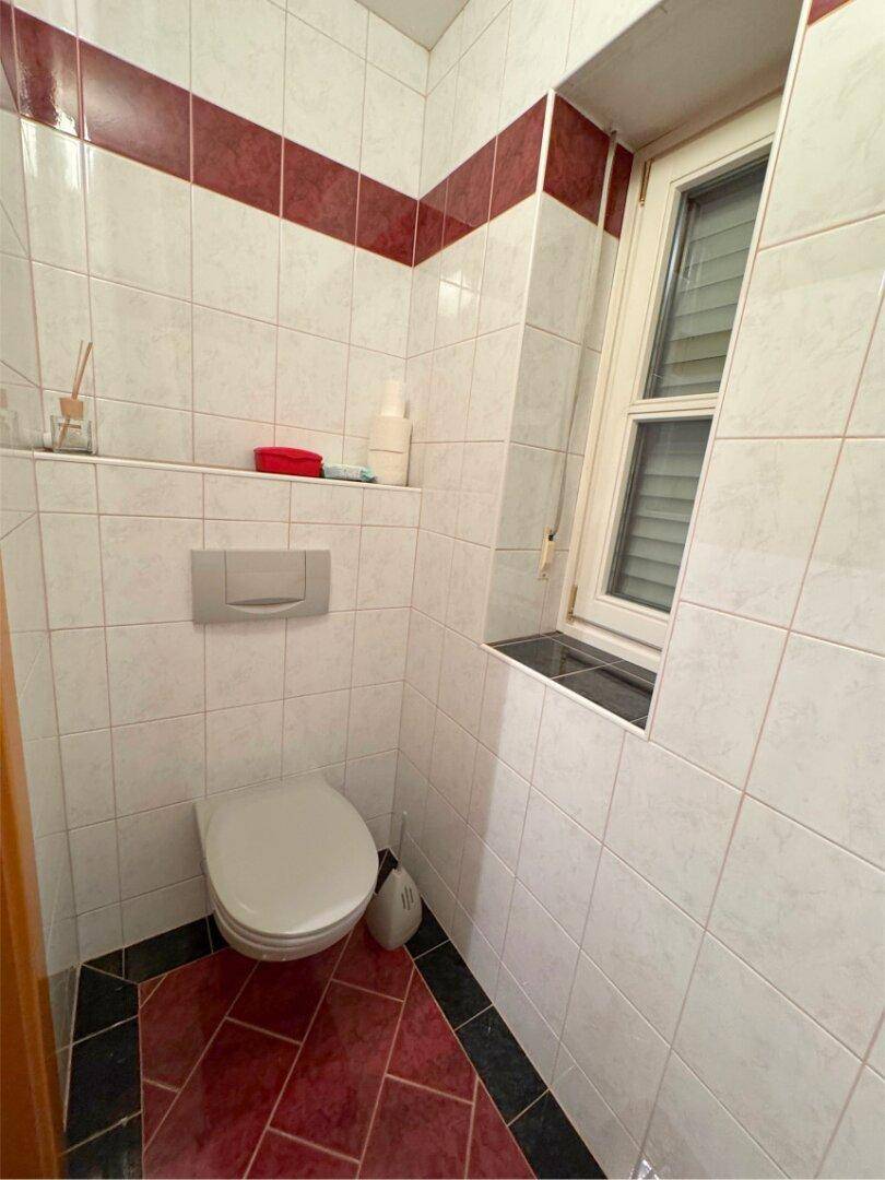 Separate Toilette mit Wand-WC, Fliesen und kleinem Fenster.