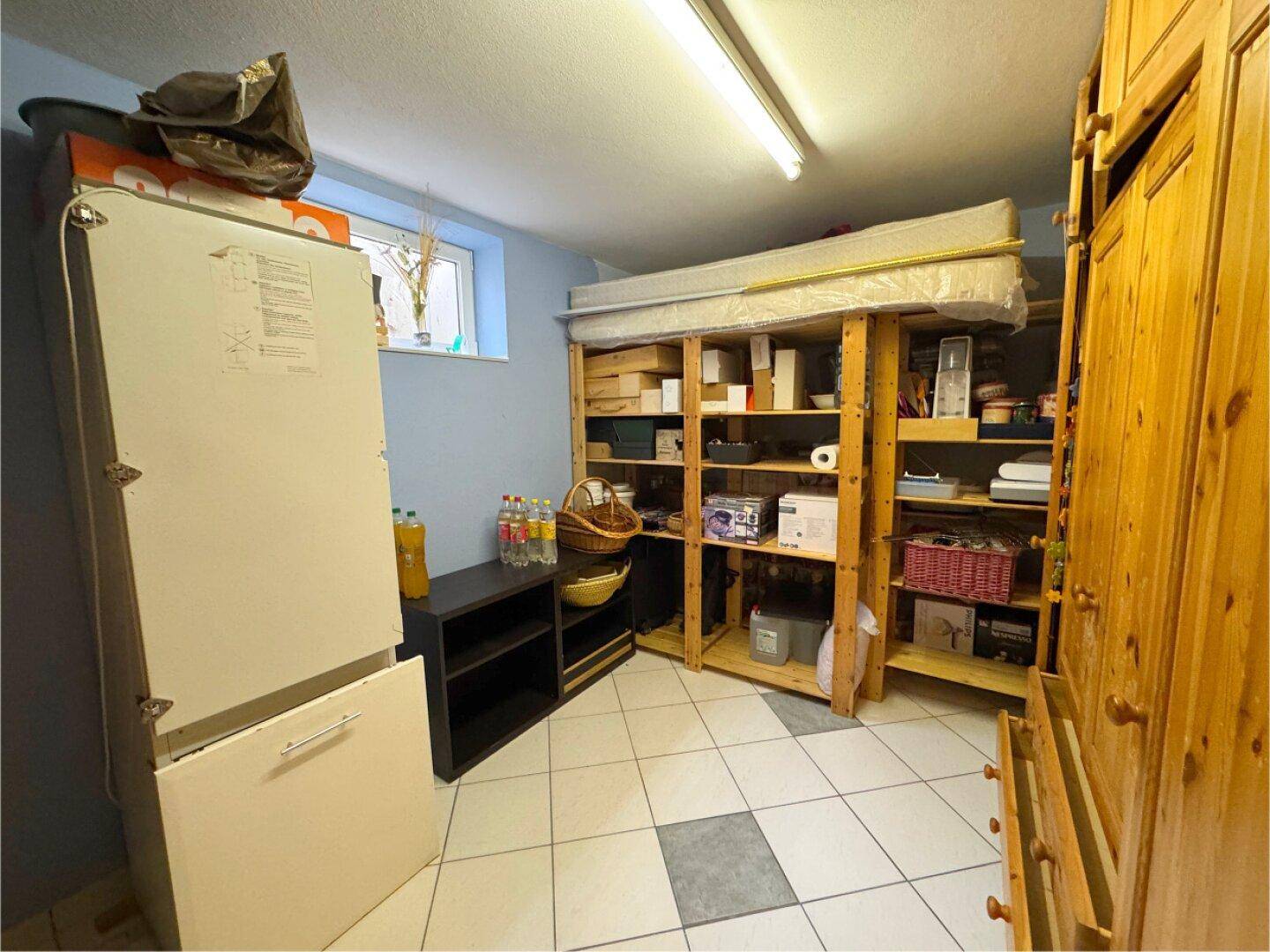 Geräumiger Lagerraum im Keller mit Regalen, Kühlschrank und kleinem Fenster.