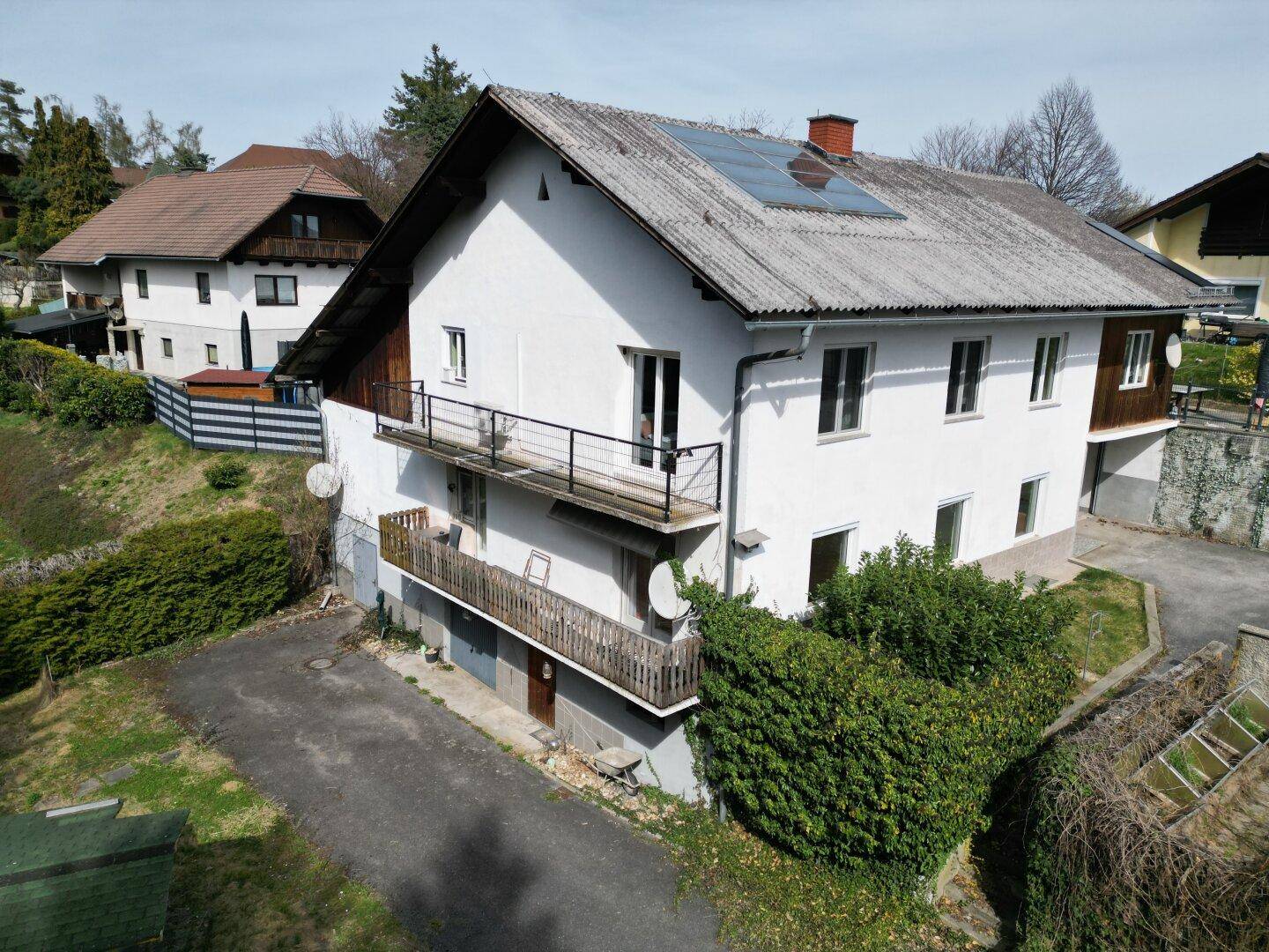 Ansicht des Wohnhauses mit zwei Balkonen und Photovoltaikanlage auf dem Dach unter blauem Himmel.
