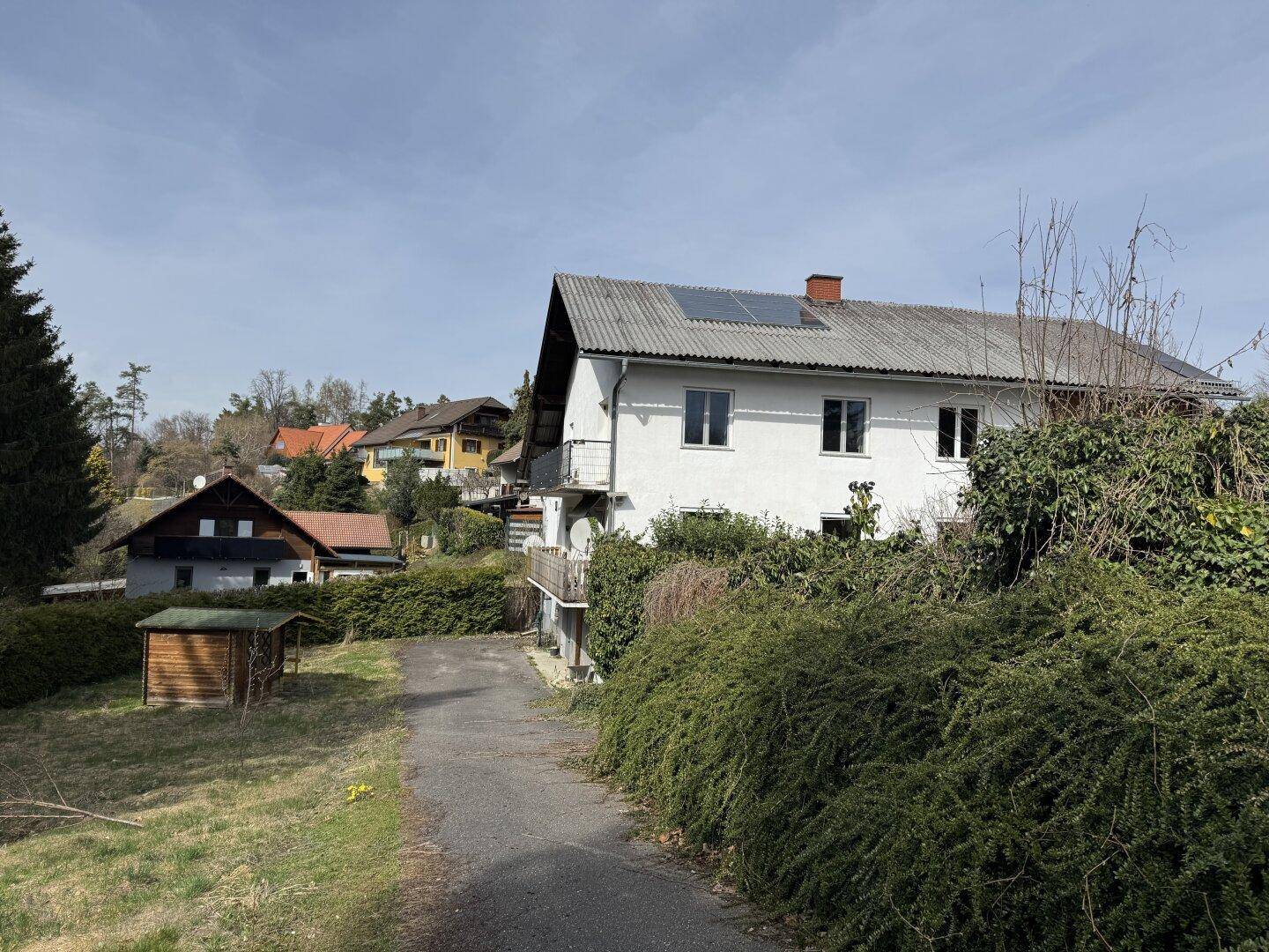 Wohnhaus mit Photovoltaikanlage auf dem Dach und gepflegter Grünfläche im Vordergrund unter blauem Himmel.