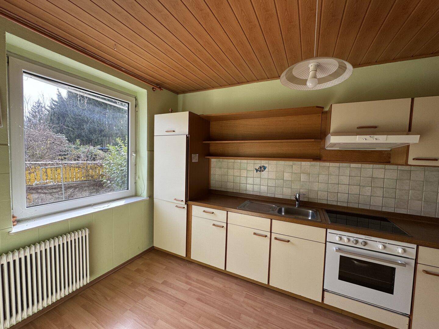 Funktionale Küche mit Holzdecke, Einbauschränken, Herd und Blick ins Grüne durch das Fenster.