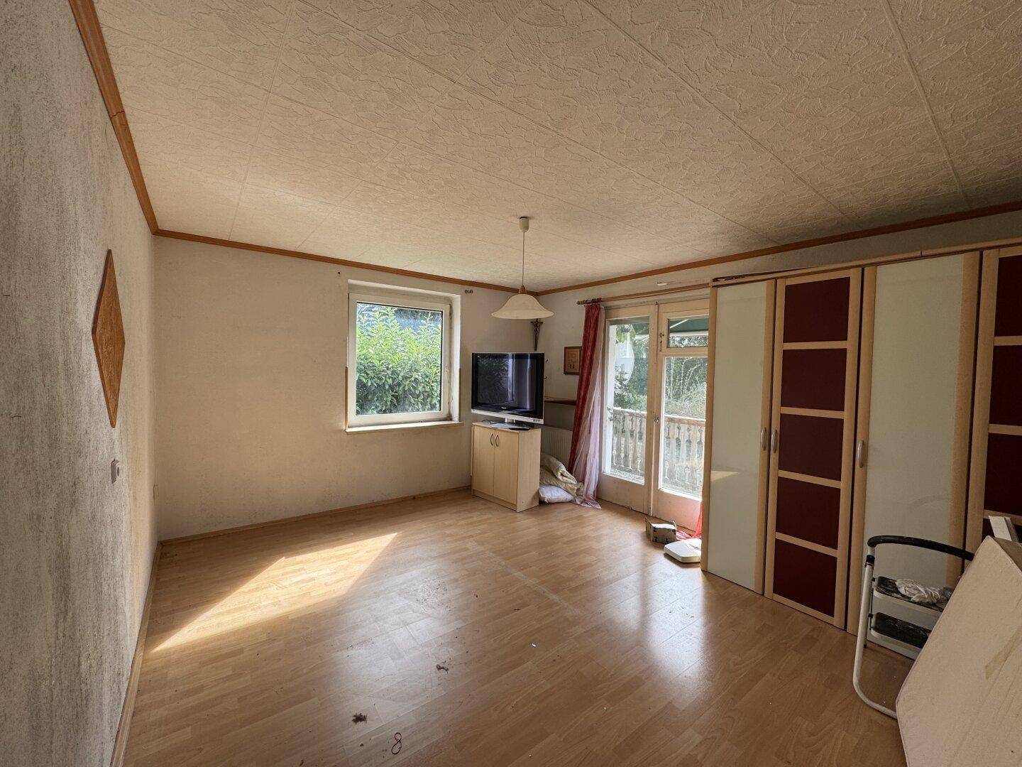 Heller Wohnraum mit Laminatboden, Zugang zum Balkon und viel Tageslicht durch große Fenster.