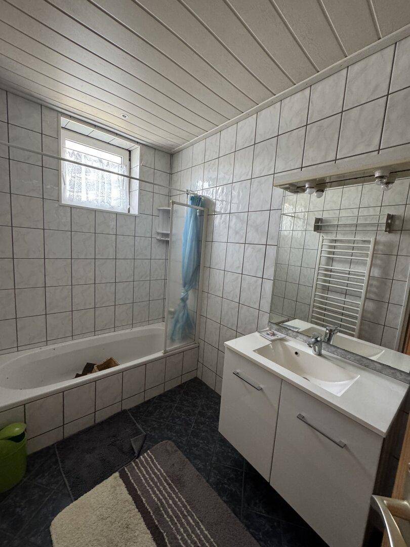 Gefliestes Badezimmer mit Badewanne, Einzelwaschbecken, Fenster und beheiztem Handtuchhalter.