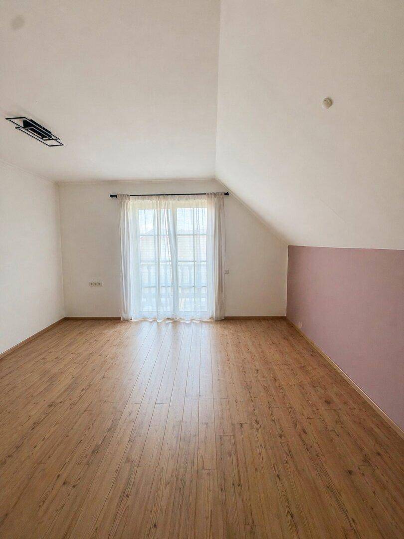 Dachgeschoss-Schlafzimmer mit Laminatboden, hellen Wänden und Zugang zu einem französischen Balkon.