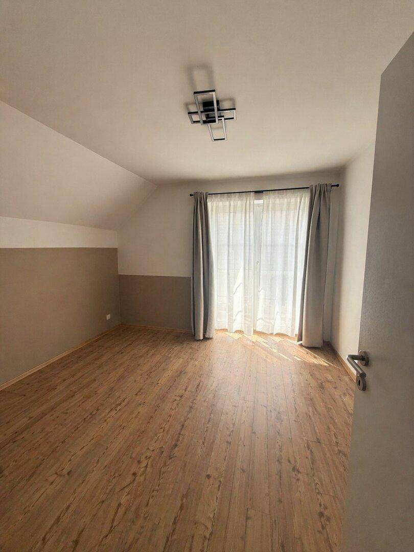 Schlafzimmer im Dachgeschoss mit Laminatboden, schrägen Wänden und Fenster mit Vorhängen.