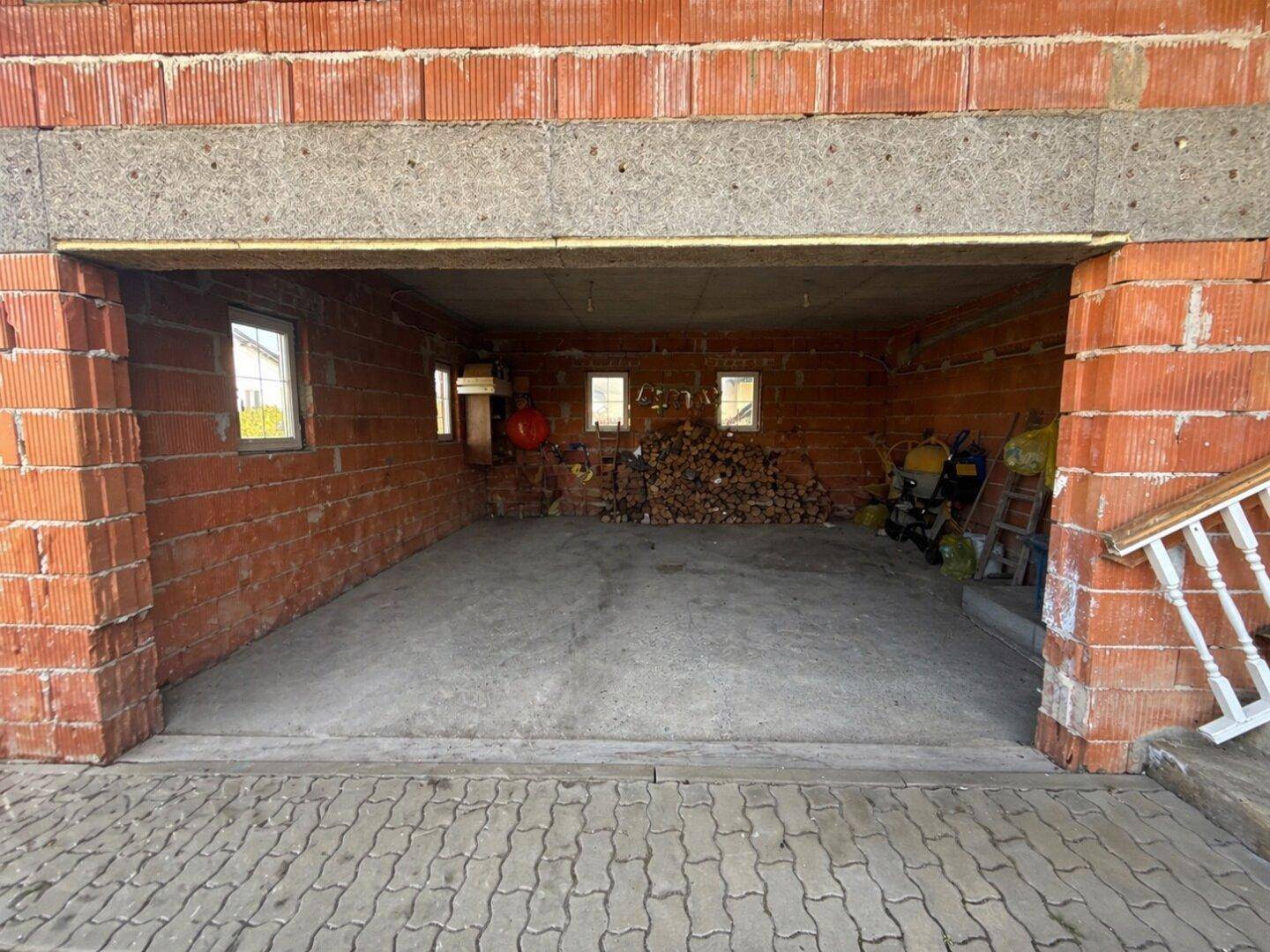 Geräumige Garage im Rohbau mit Ziegelwänden und Betonboden.