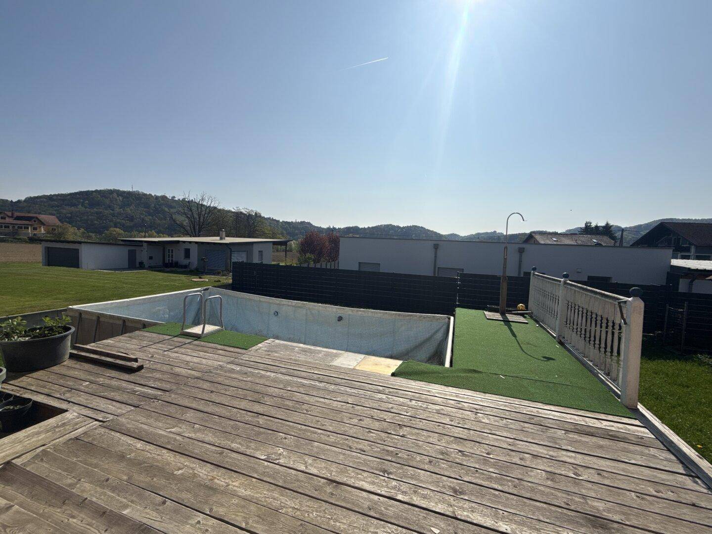 Holzterrasse mit Poolbereich und Blick auf die grüne Umgebung unter strahlendem Sonnenschein.