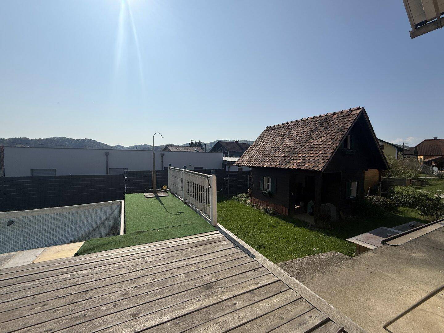 Holzterrasse mit Pool und angrenzendem Gartenbereich unter blauem Himmel.