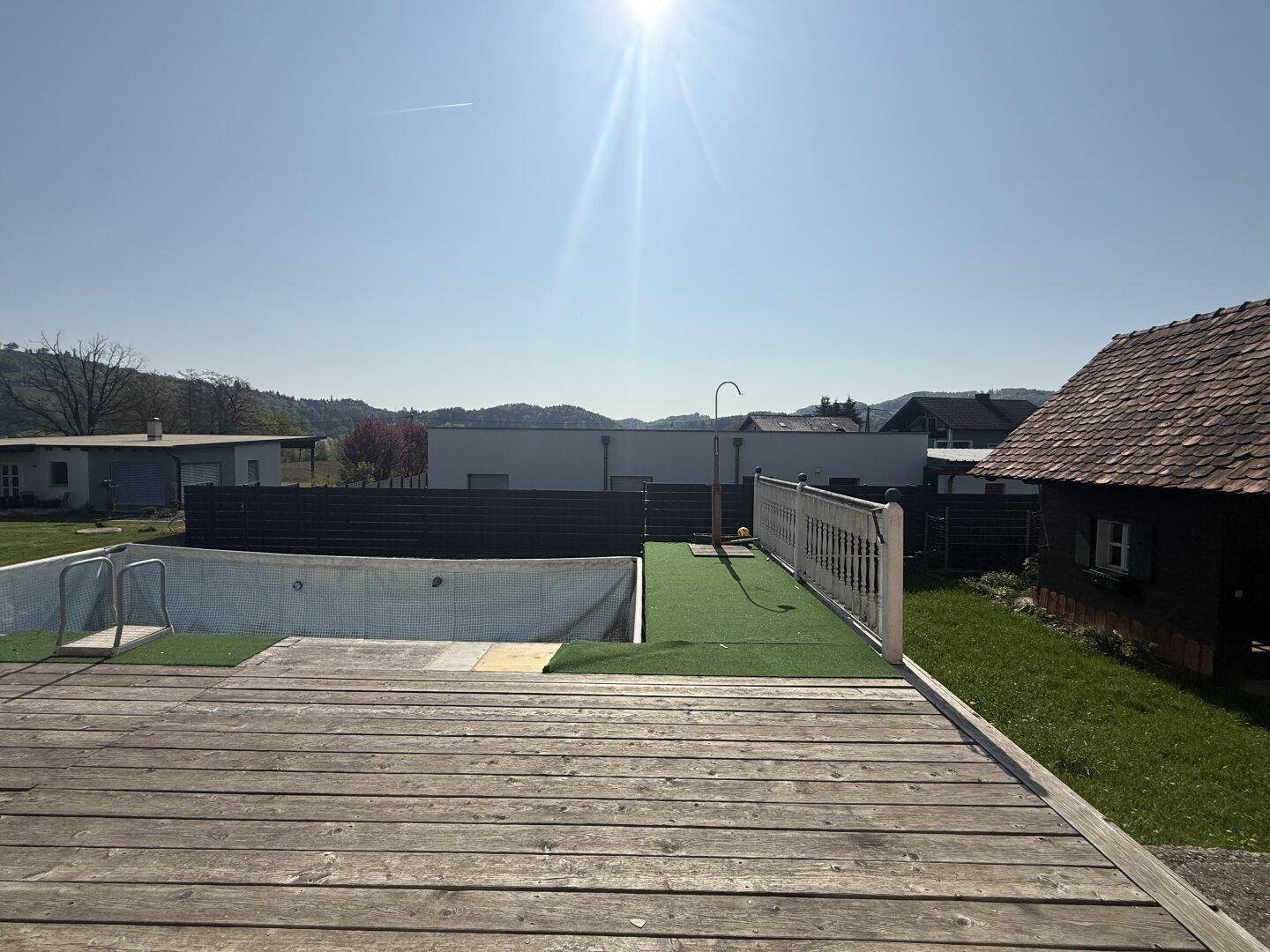 Holzterrasse mit eingelassenem Pool und Blick auf die umliegende Landschaft unter blauem Himmel.