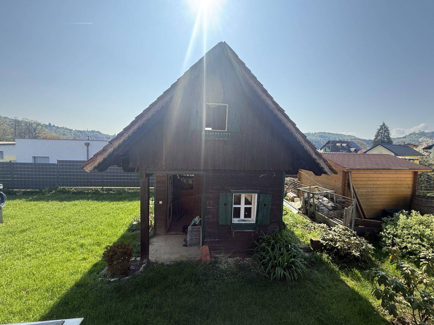 Grüner Gartenbereich mit einem kleinen Holzhaus und Blick auf die Umgebung.
