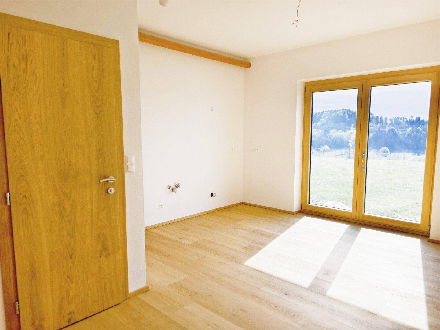Heller Raum mit Holzboden, großen Fenstern und Zugang zu einem Außenbereich, ideal für Wohnzwecke.