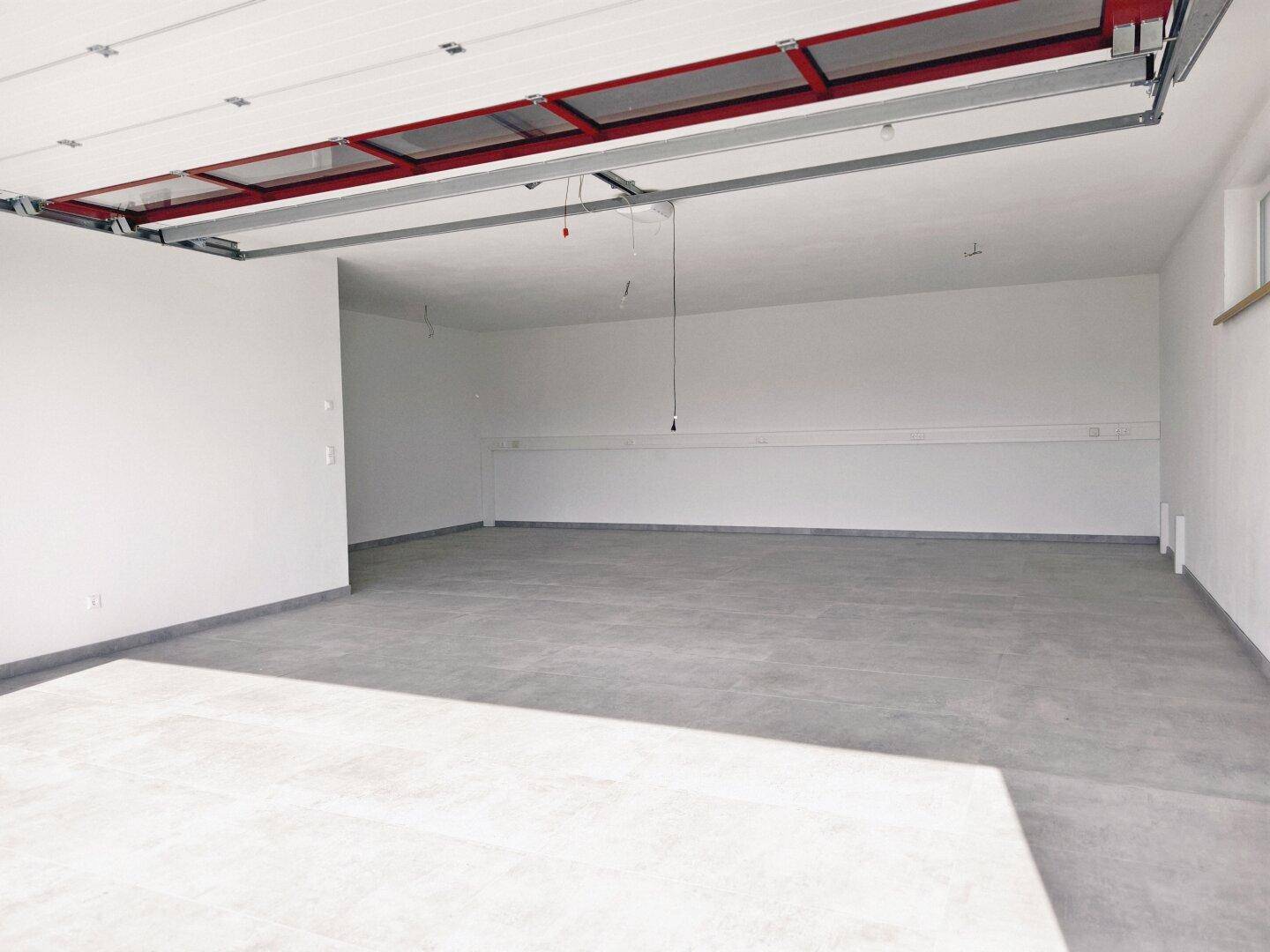 Geräumige Garage mit Betonboden und automatischem Garagentor, bereit für Fahrzeuge.