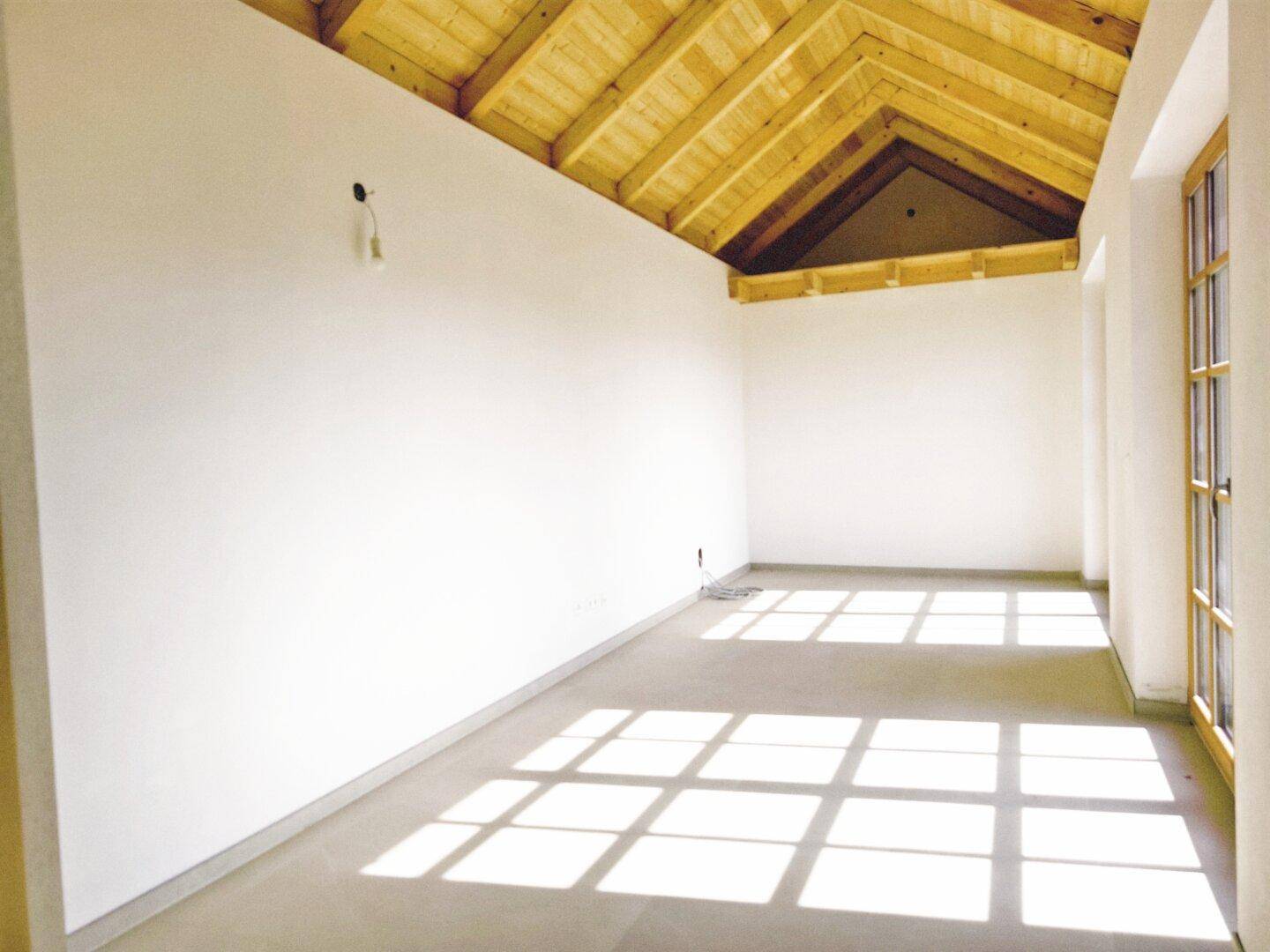 Heller Dachraum mit sichtbarer Holzdecke und großen Fenstern, bereit zum Ausbau.