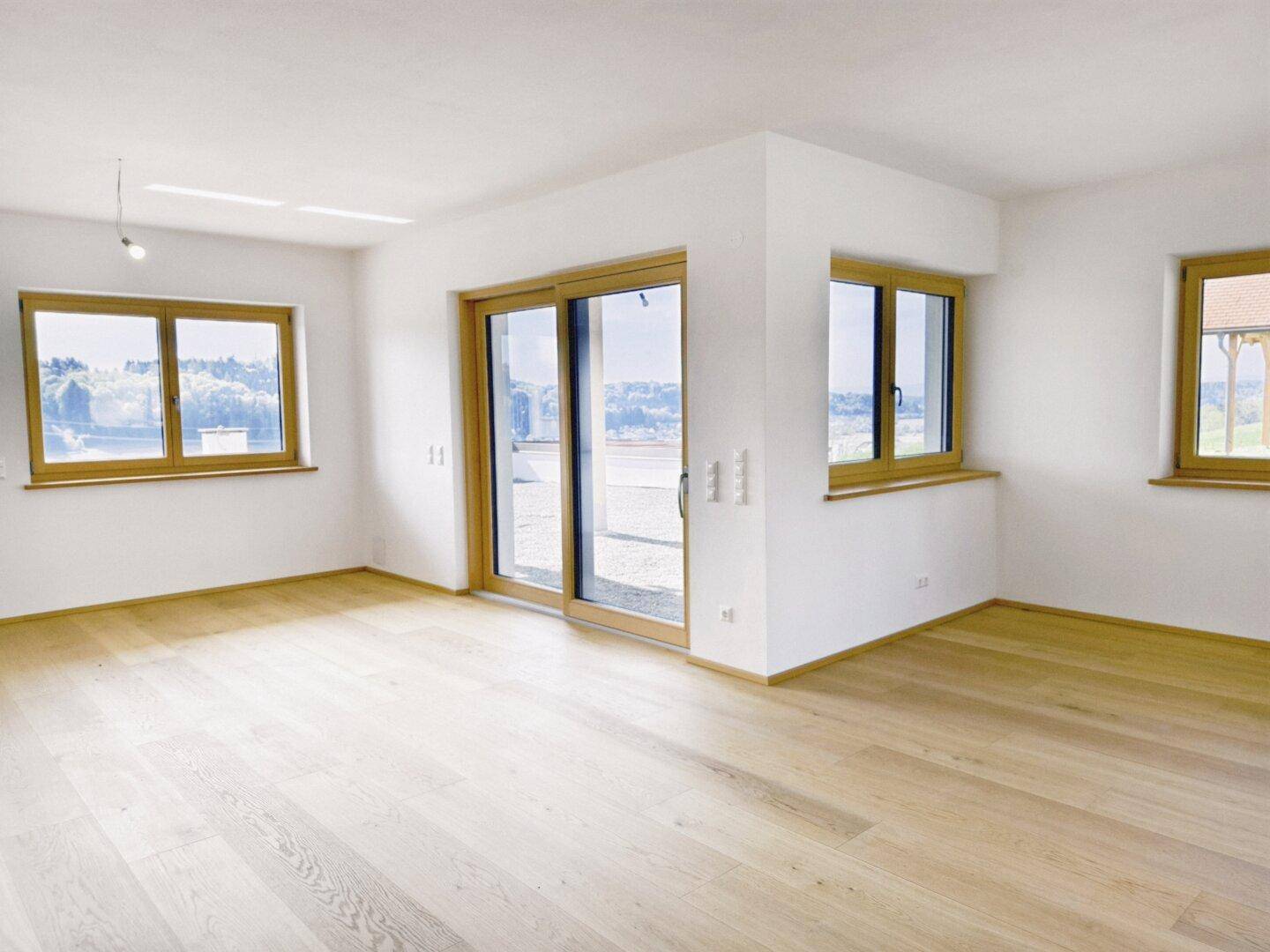 Geräumiger, heller Wohnbereich mit Holzboden und großen Fenstern, die viel Tageslicht hereinlassen.
