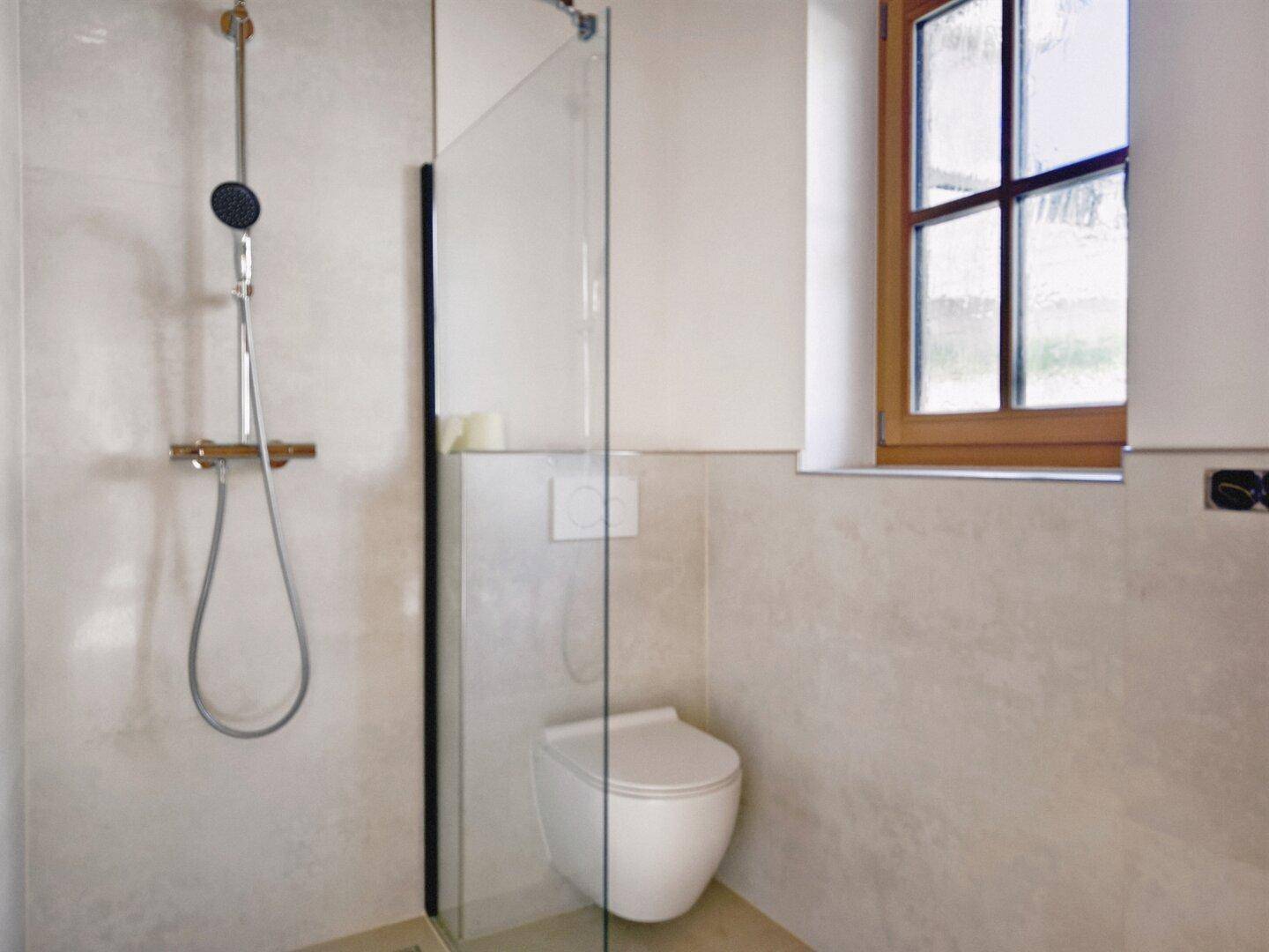 Modernes Badezimmer mit begehbarer Dusche, Wand-WC und kleinem Fenster für Tageslicht.