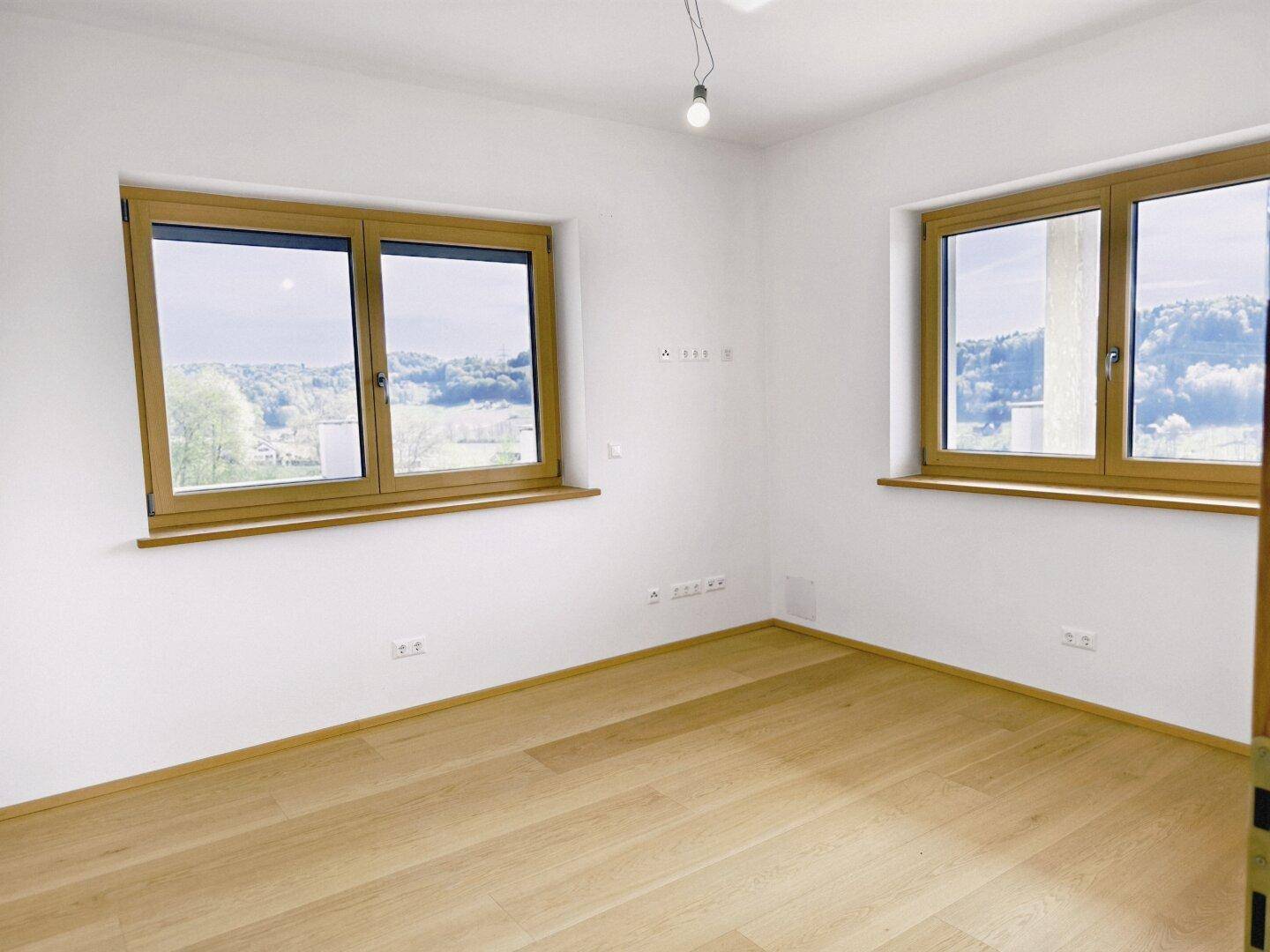 Helles Schlafzimmer mit Holzboden und großen Fenstern, die einen weiten Blick in die Natur bieten.