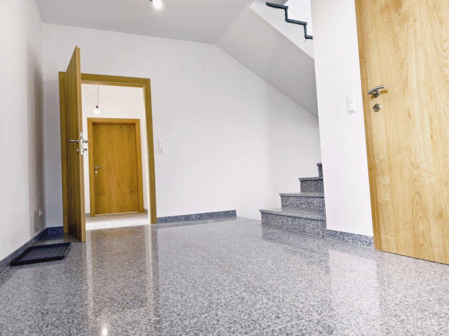 Geräumiger Eingangsbereich mit glänzendem Fliesenboden und Treppe zum Obergeschoss.