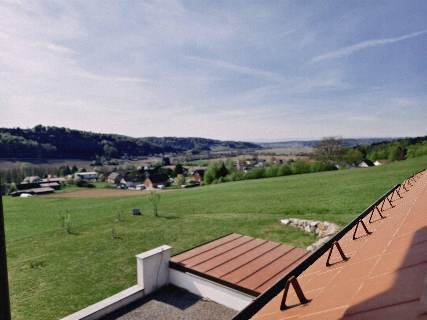 Panoramablick von der Terrasse über die ländliche Umgebung mit Feldern und Wäldern unter blauem Himmel.