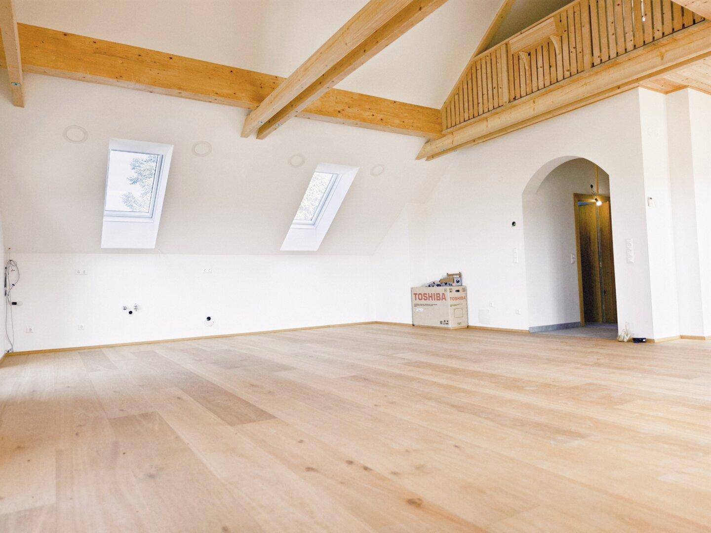 Geräumiger Dachgeschossraum mit Holzboden, Dachfenstern und sichtbaren Holzbalken, bereit zum Ausbau.