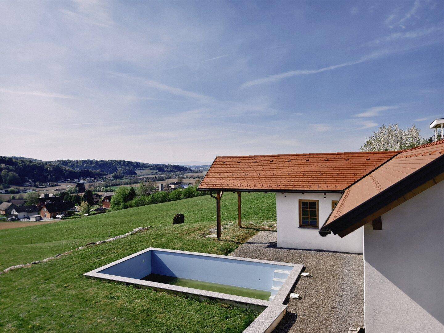 Außenbereich mit eingelassenem Pool und einem Nebengebäude, umgeben von grüner Wiese.