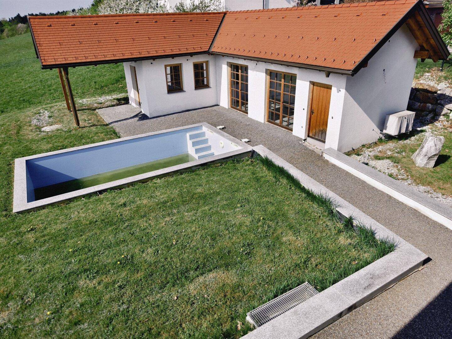 Außenbereich mit eingelassenem Pool, Nebengebäude und Zugang über eine Rampe.