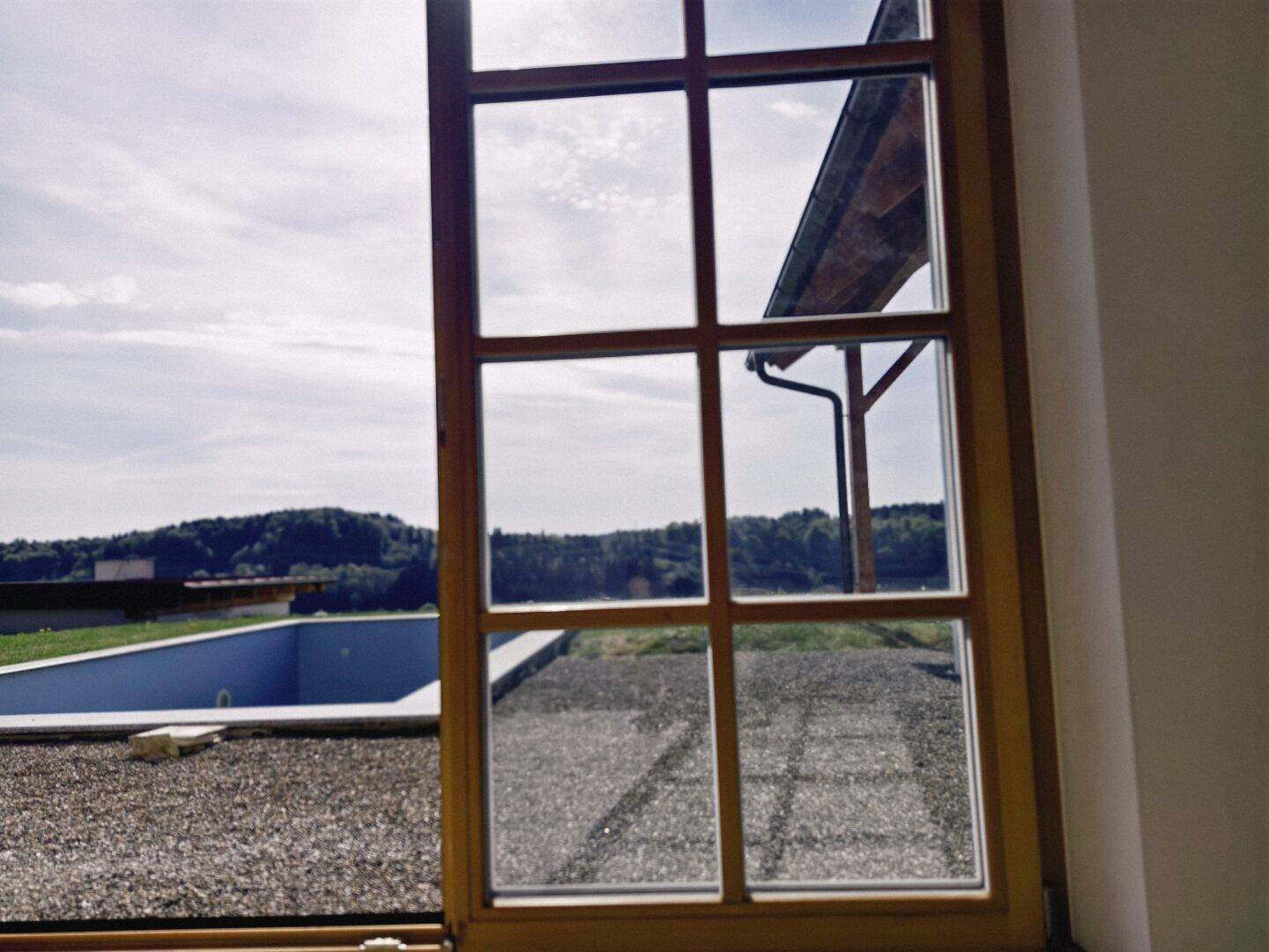 Ausblick aus einem Fenster auf den Poolbereich und die umliegende Landschaft.