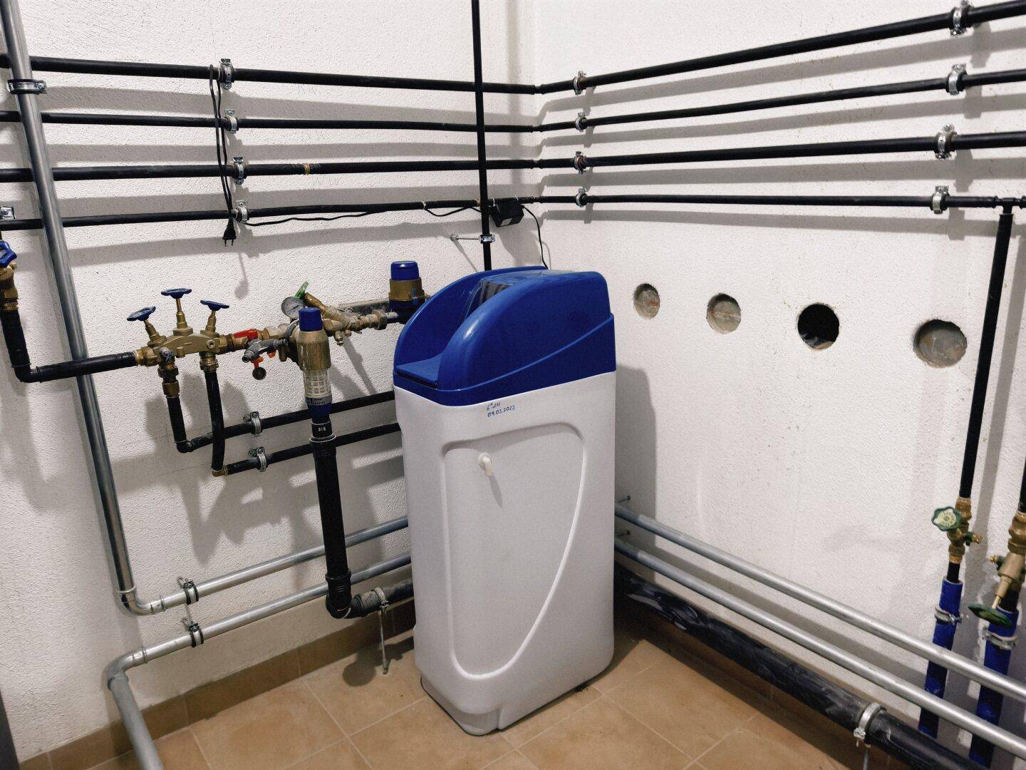 Technikraum mit Wasseraufbereitungsanlage und umfangreichen Rohrleitungen an der Wand.