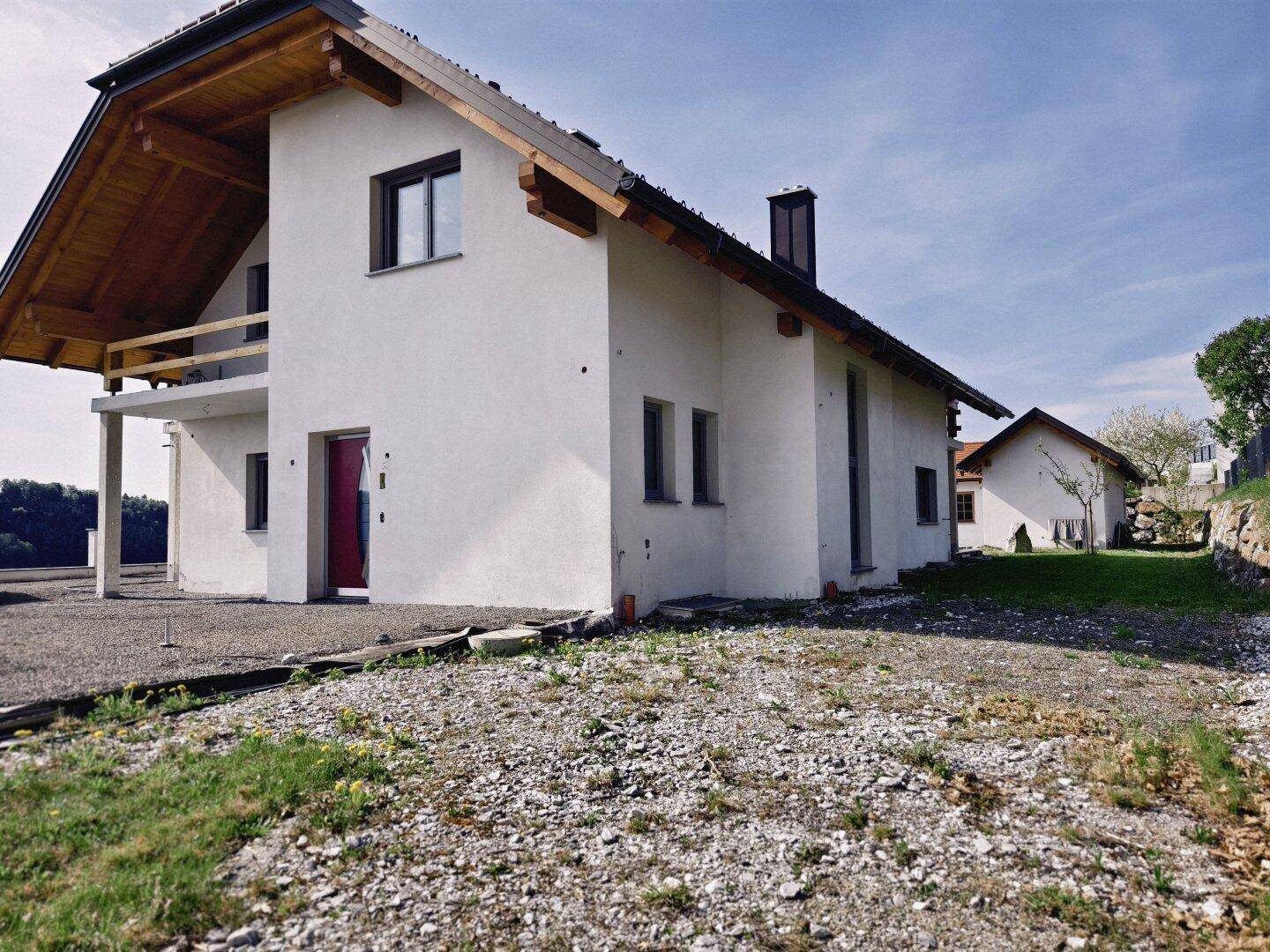 Seitenansicht des modernen Wohnhauses mit weißer Fassade und Holzelementen unter blauem Himmel.