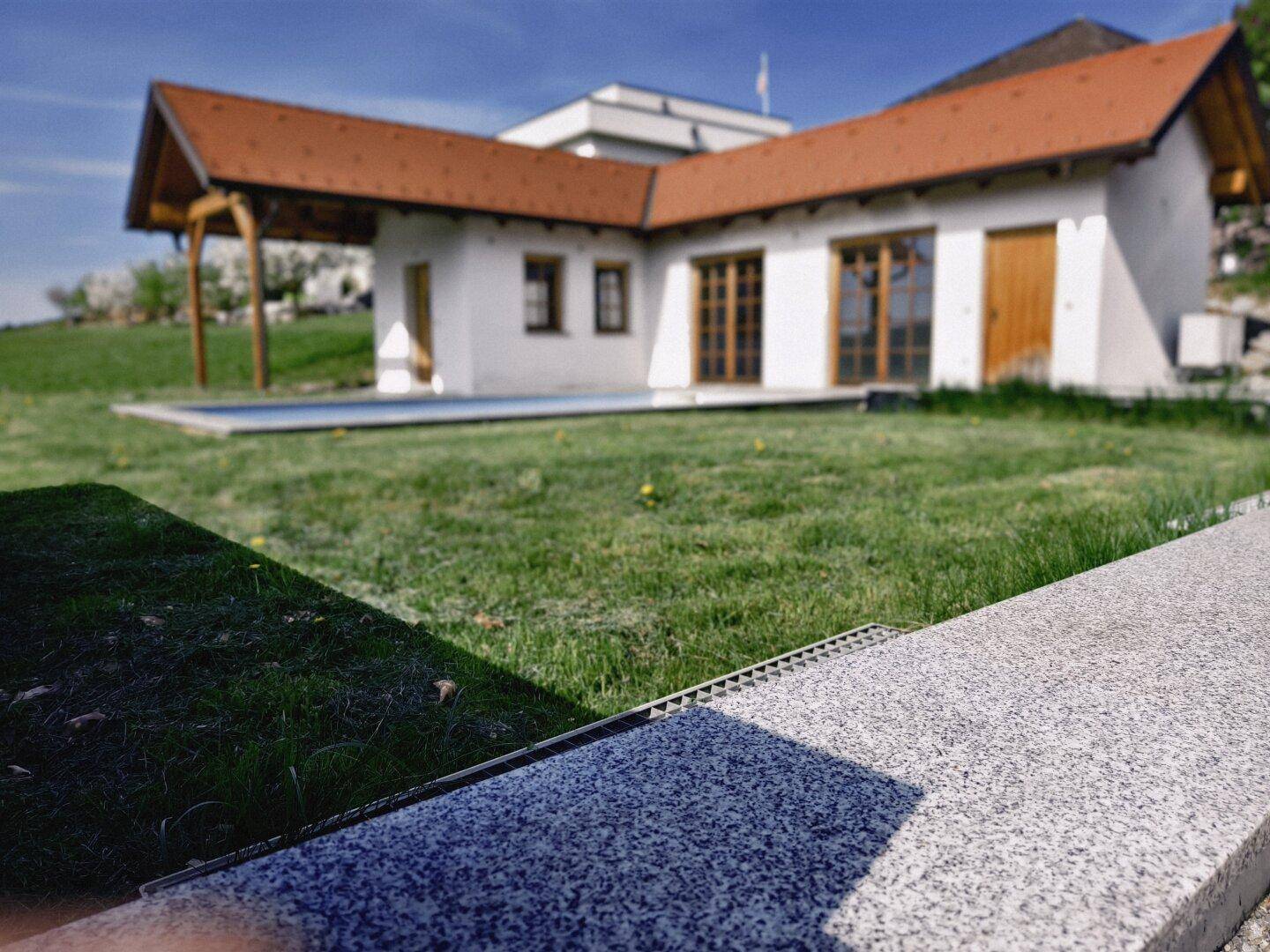 Außenbereich mit eingelassenem Pool und Nebengebäude, umgeben von grüner Wiese.