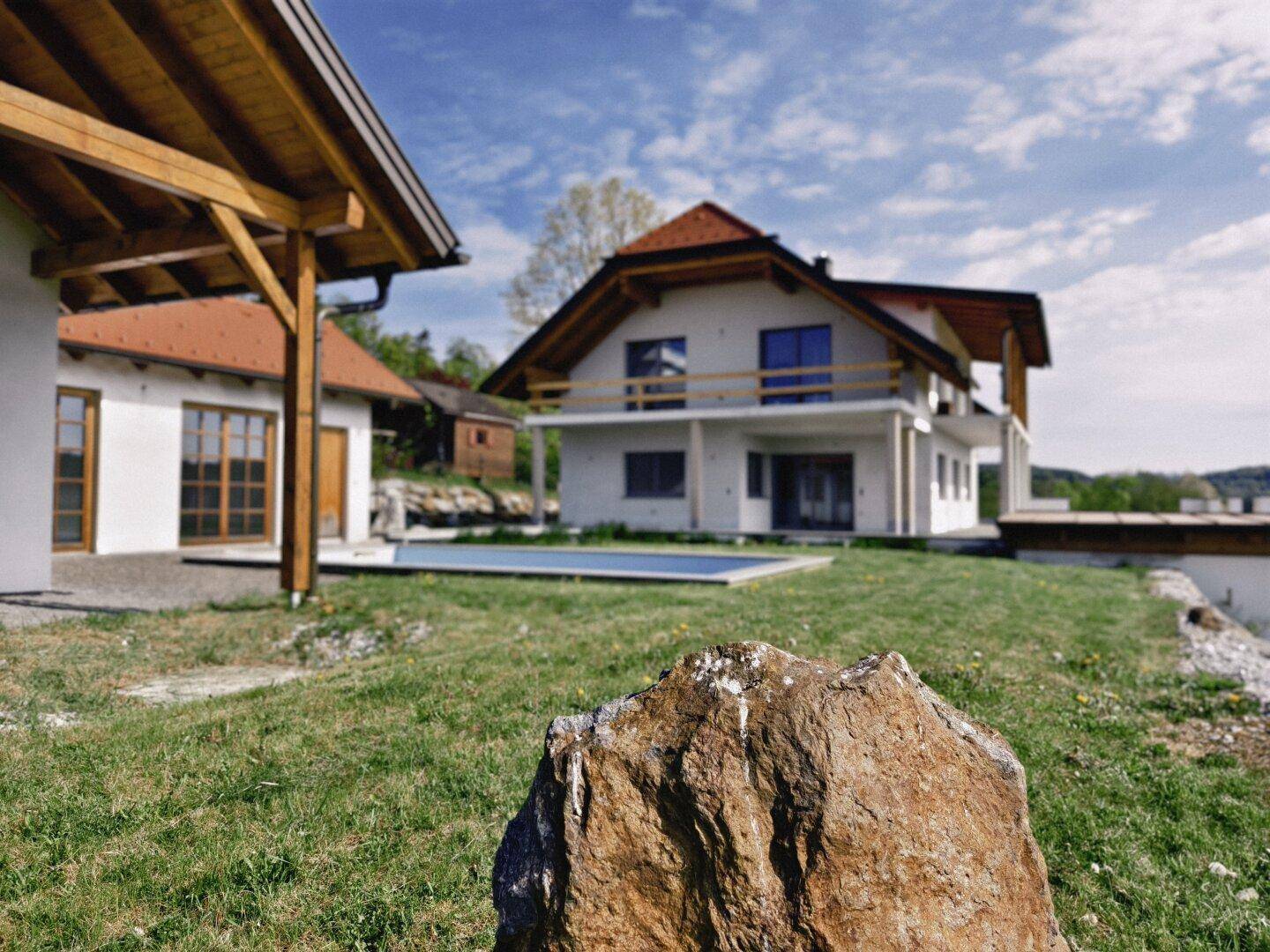 Modernes Wohnhaus mit Nebengebäude, Pool und weitläufiger Grünfläche, umgeben von Natur.