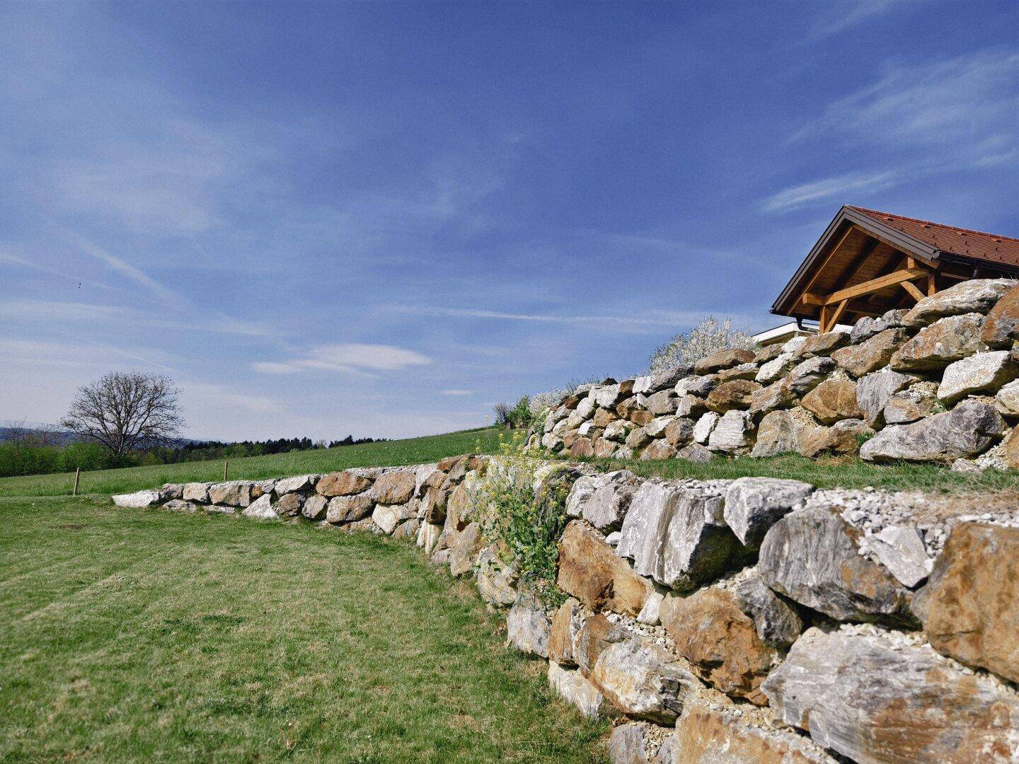 Beeindruckende Trockenmauer aus Natursteinen, die sich harmonisch in die grüne Landschaft einfügt.