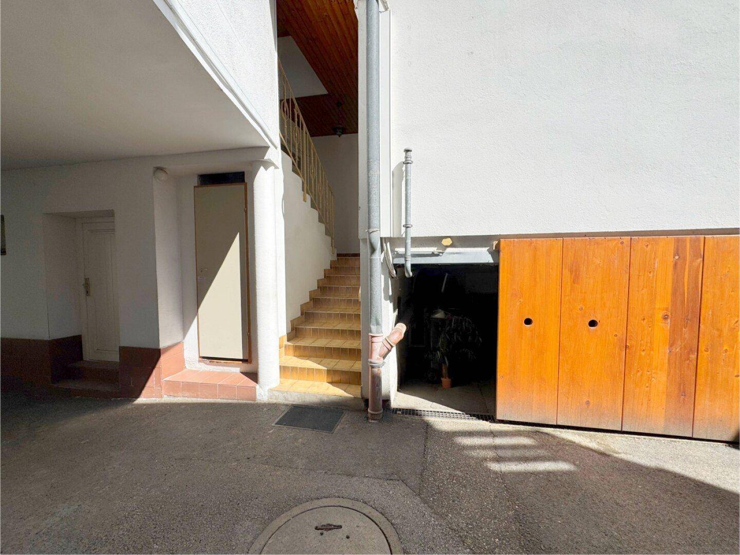 Garagenzufahrt mit Holztor und Außentreppe, die zu den oberen Wohneinheiten führt.