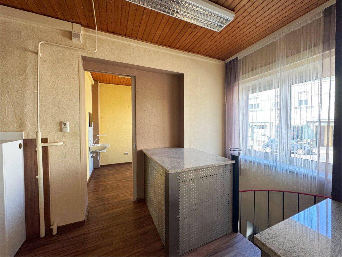 Übergangsbereich mit Holzdecke, Fenster und einem kleinen Waschbecken im Hintergrund.
