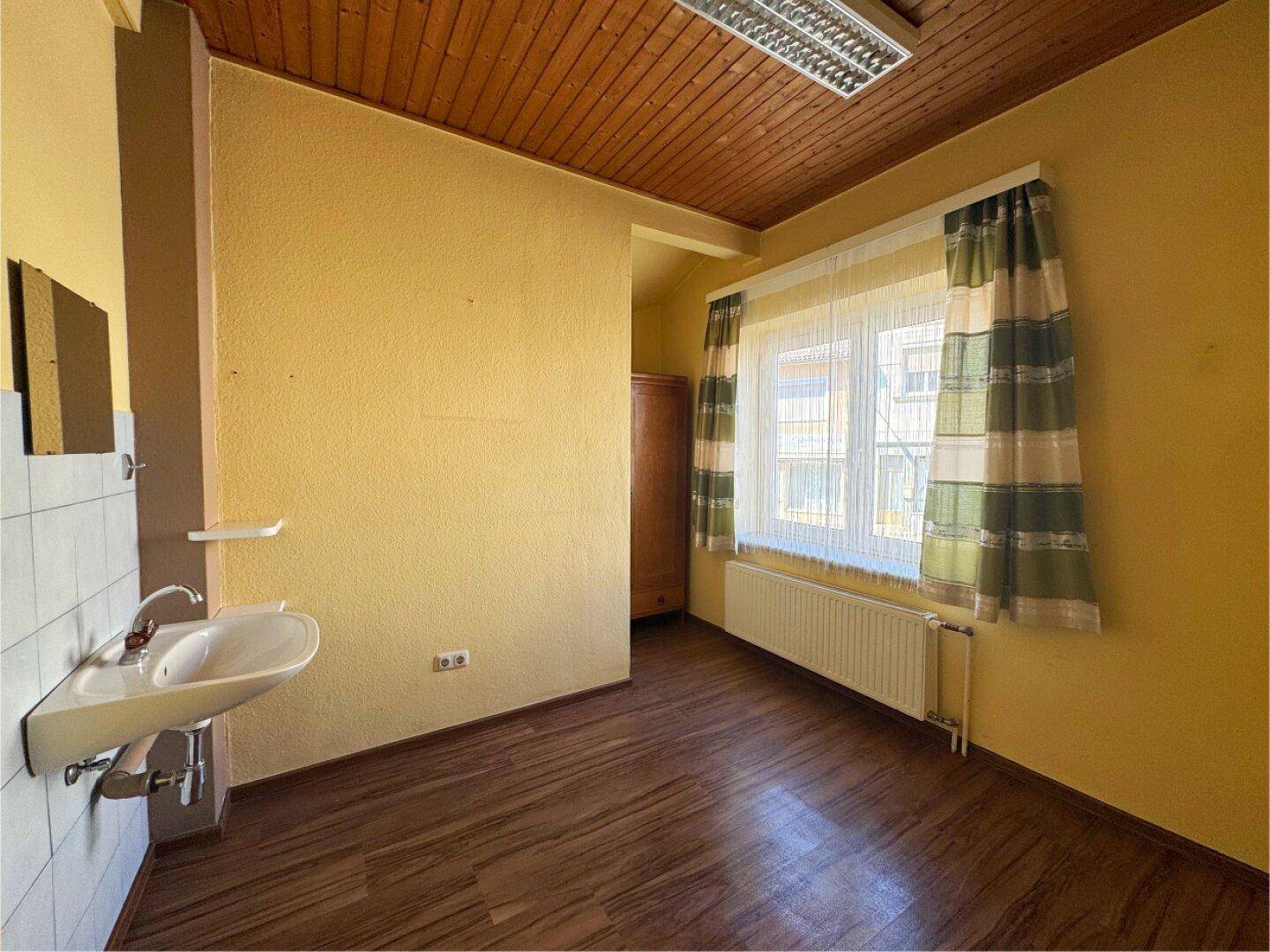 Raum mit gelben Wänden, Holzdecke, Fenster und einem Waschbecken an der Seite.