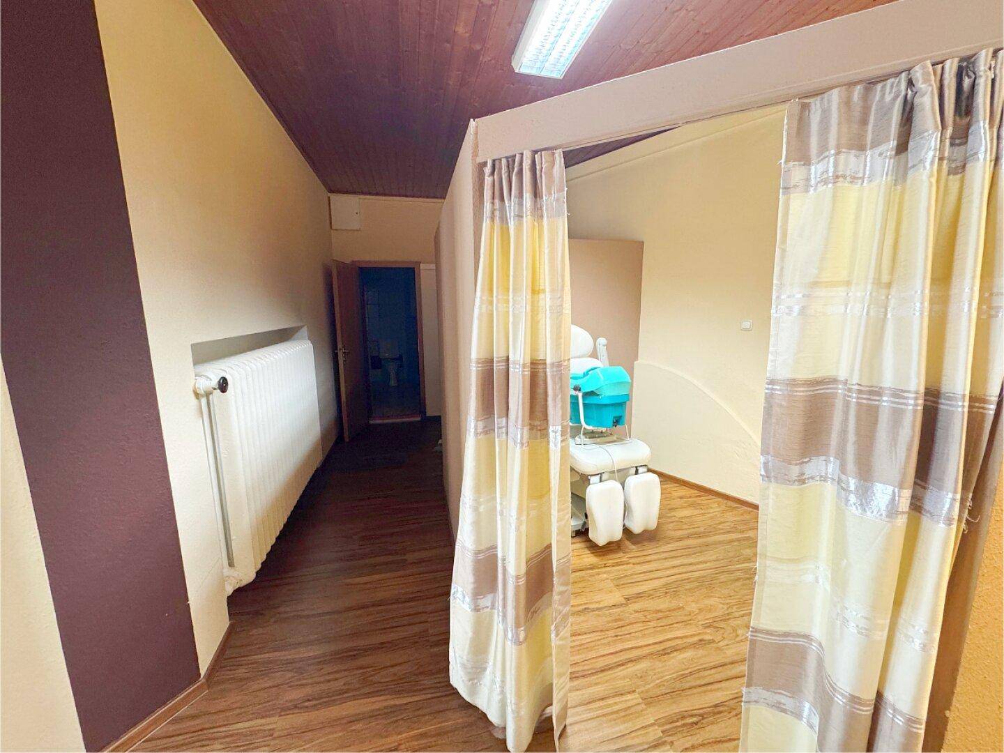 Behandlungsraum mit Vorhangabtrennung, Holzfußboden und einem Behandlungsstuhl.