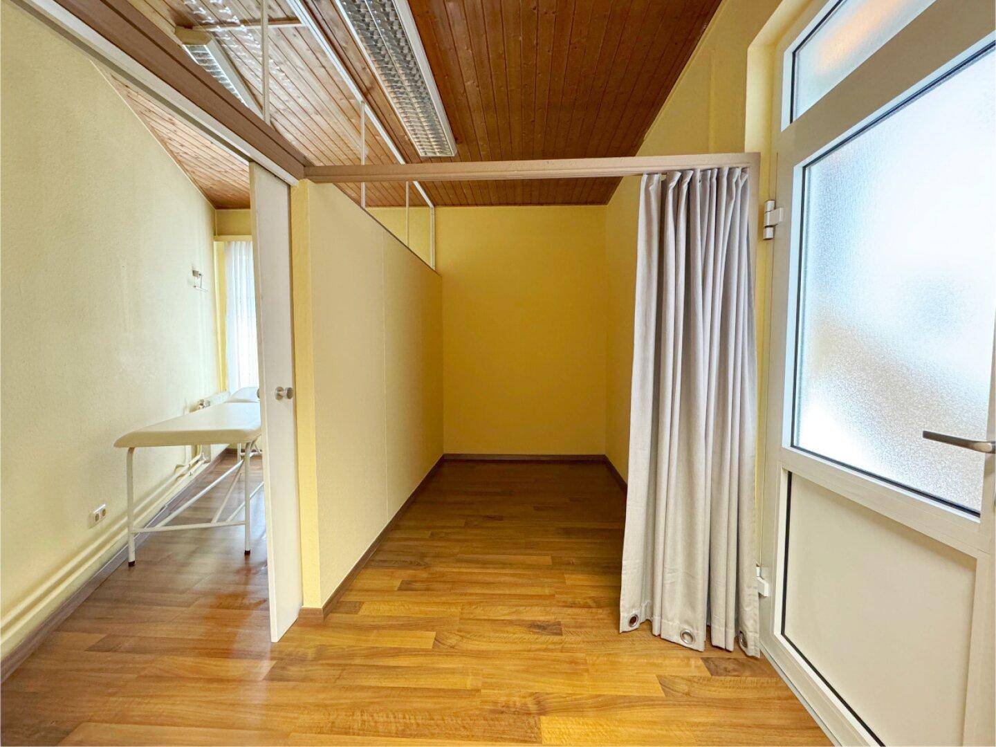 Innenraum mit gelben Wänden, Holzdecke und einem Vorhang, der einen Bereich abtrennt.