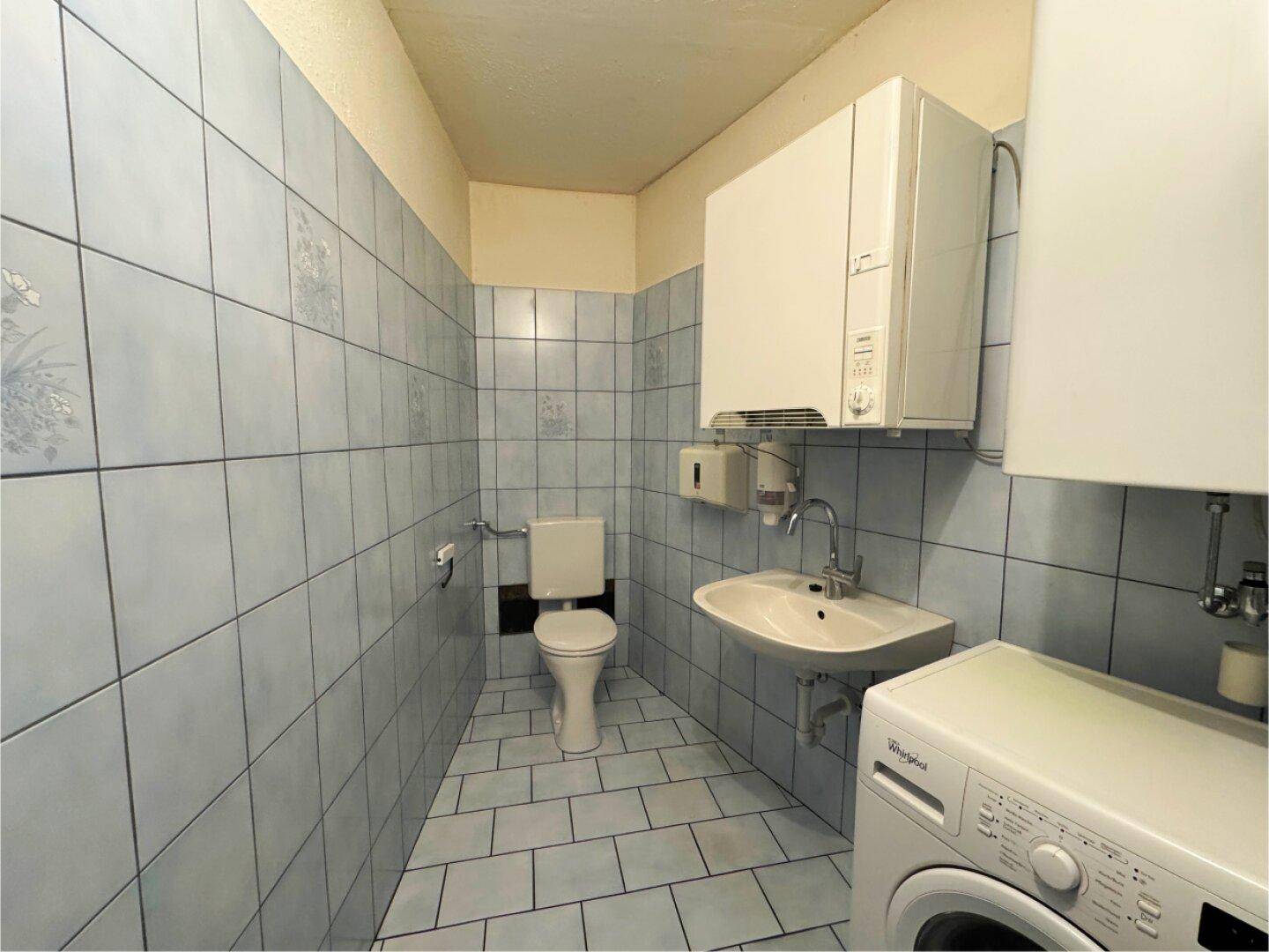 Badezimmer mit hellblauen Fliesen, Toilette, Waschbecken und Waschmaschine.