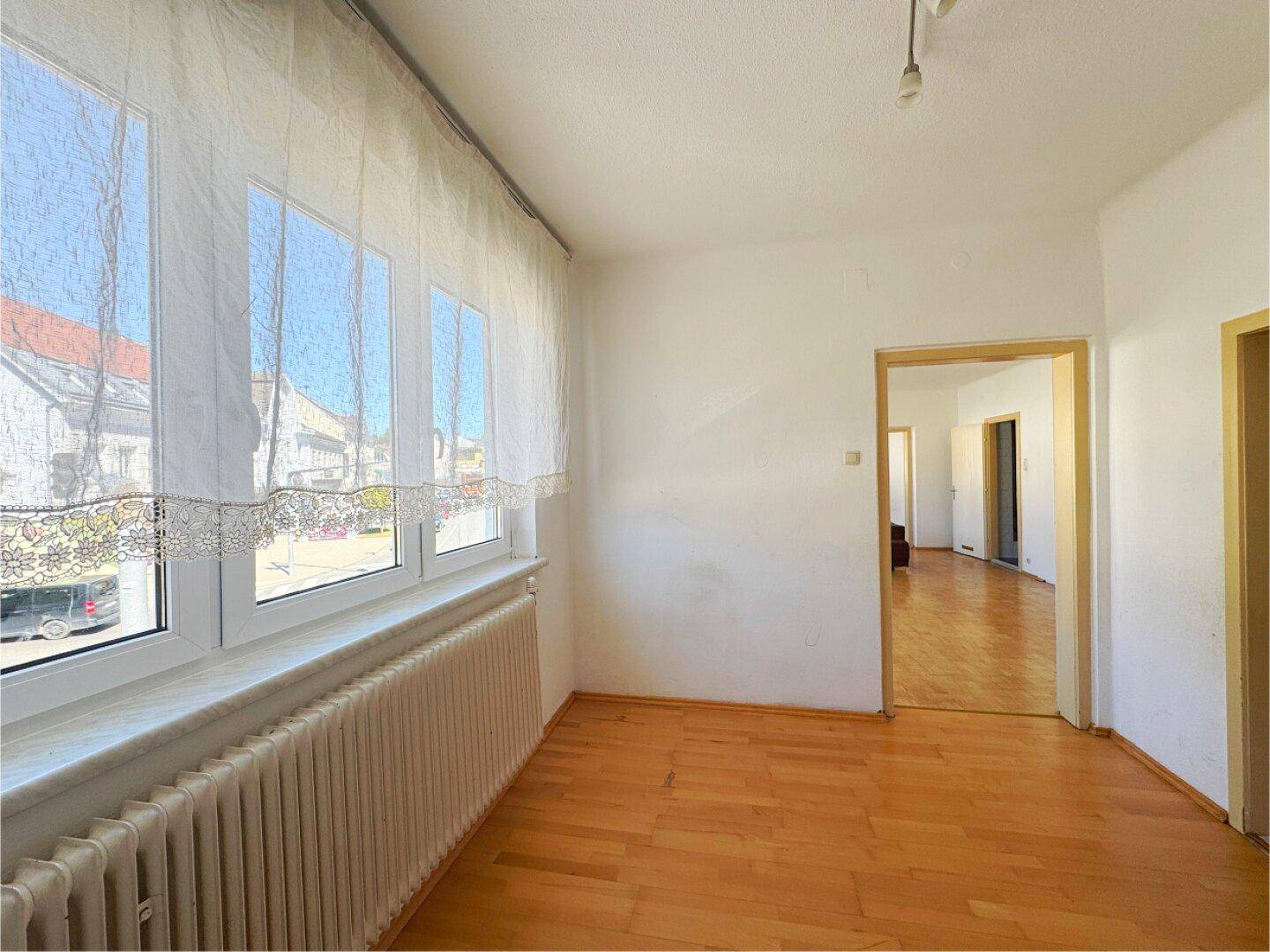 Heller Raum mit Parkettboden und großen Fenstern, die viel Tageslicht hereinlassen.