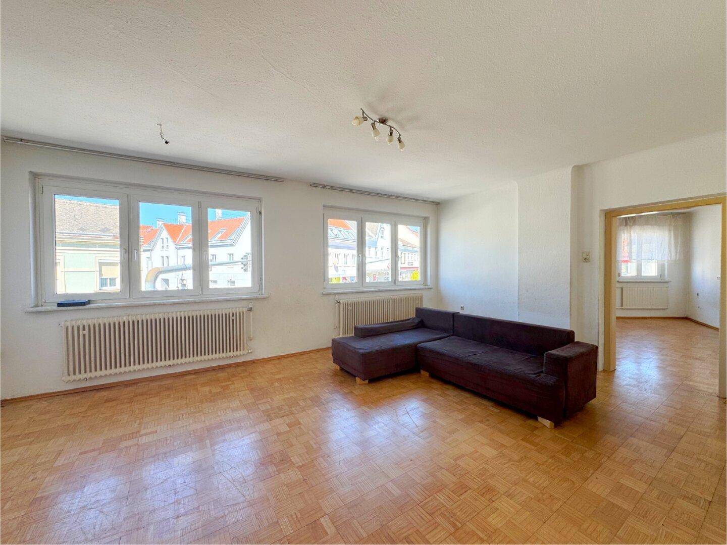 Helles Wohnzimmer mit Parkettboden, großen Fenstern und einem Sofa.