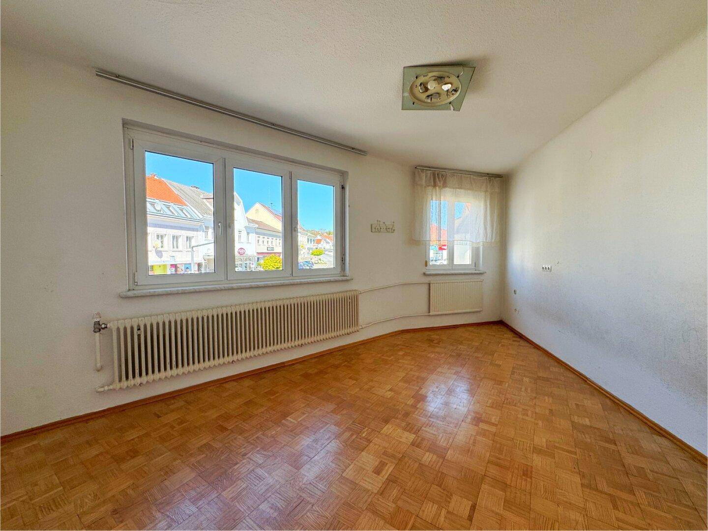Geräumiger Raum mit Parkettboden und großen Fenstern, ideal für Wohnzwecke.