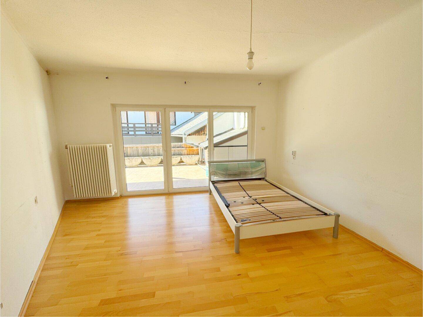 Schlafzimmer mit hellem Holzboden und Zugang zu einem Außenbereich durch eine Schiebetür.