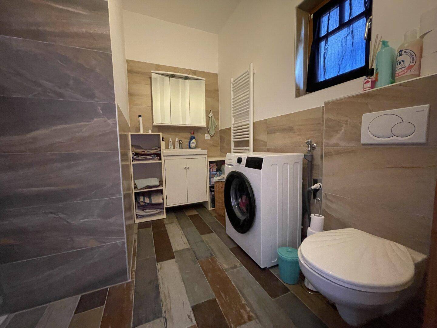 Modern gefliestes Badezimmer mit Toilette, Waschbecken und Waschmaschine.