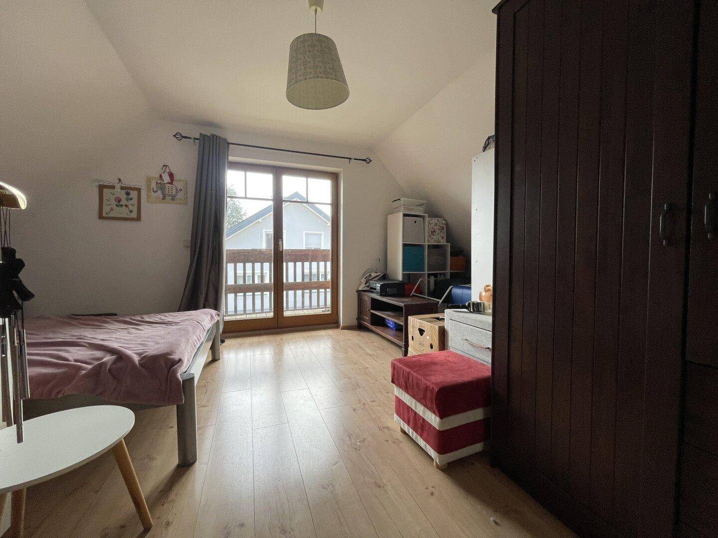 Schlafzimmer im Dachgeschoss mit Zugang zum Balkon und Holzboden.