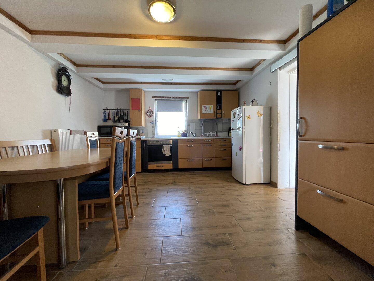 Geräumige Küche mit Essbereich, Holzschränken, Fliesenboden und sichtbaren Deckenbalken.