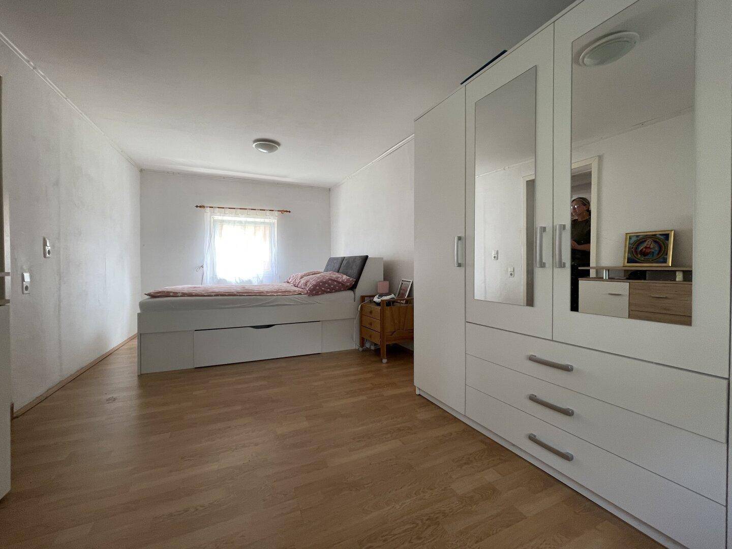 Weiterer Blick ins Schlafzimmer mit Bett, Fenster und großem weißen Kleiderschrank mit Spiegelflächen.