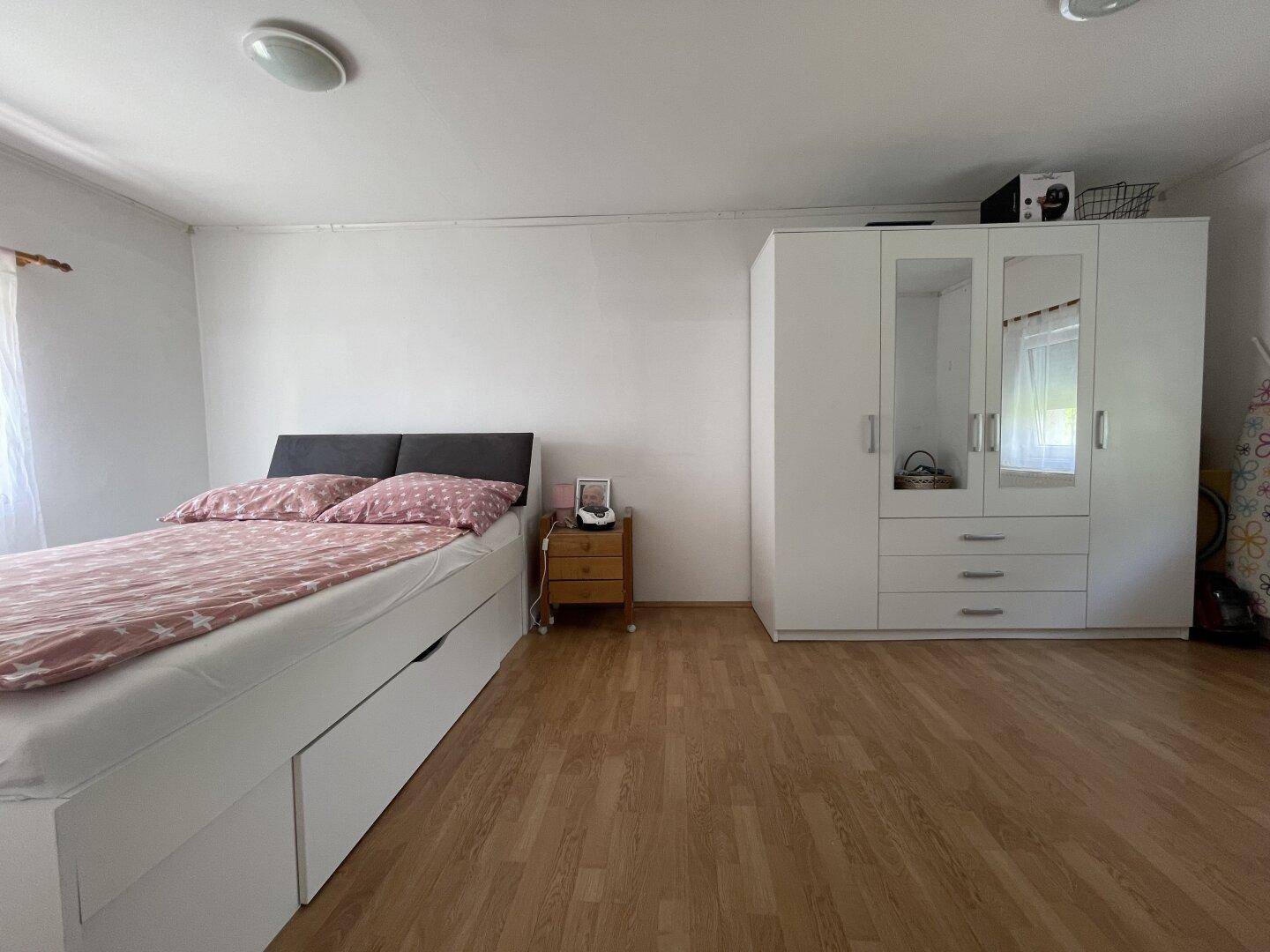Schlafzimmer mit Bett mit Stauraum, Nachttisch und weißem Kleiderschrank mit Spiegeltüren.
