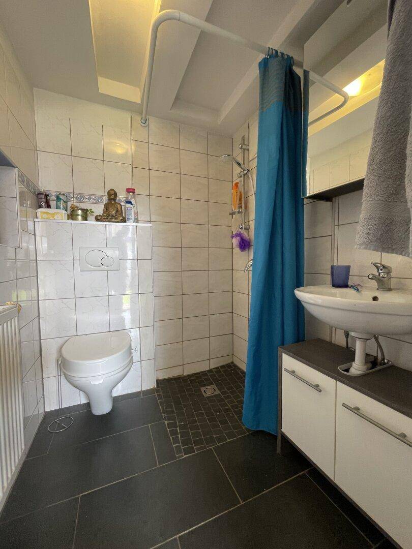 Badezimmer mit WC, Waschbecken mit Unterschrank und Duschbereich mit blauer Duschvorhang.