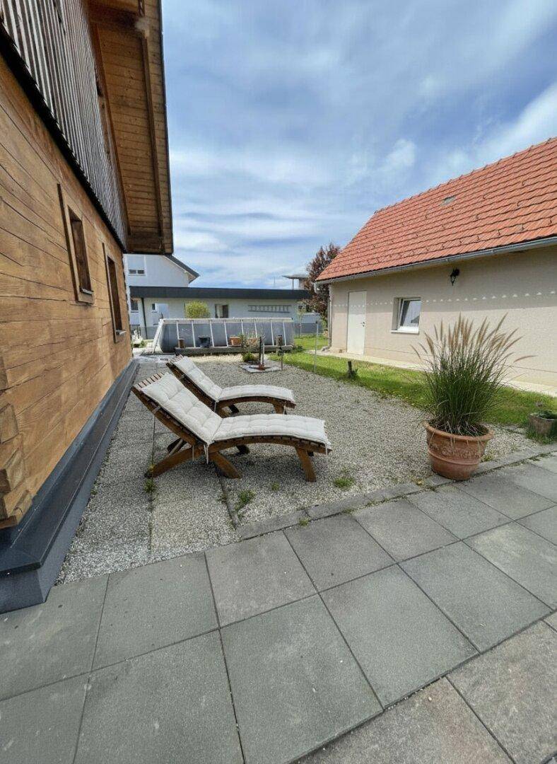 Entspannungsbereich im Garten mit Liegestühlen auf Kies und Blick auf das Nachbargebäude.